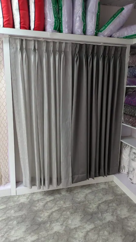 Grey striped sheer and charcoal blackout pinch-pleat curtain samples hanging on the showroom display rail