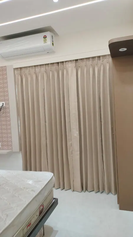 Beige herringbone pinch-pleat curtains running floor to ceiling beside a fitted wardrobe