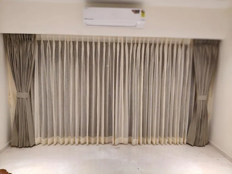 Double-layer window treatment — grey sheers behind taupe side curtains with matching tie-backs