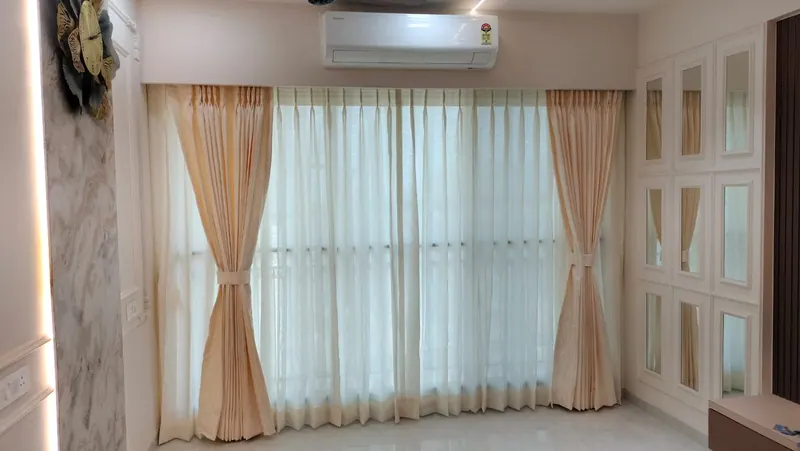 Peach pinch-pleat curtains layered over white sheers with fabric tie-backs in a Thane living room