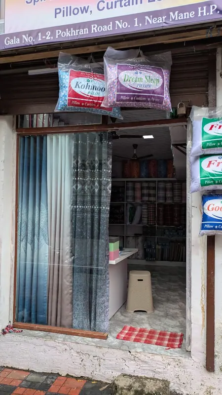 Entrance of Gouri Mattresses & Furnishing showing curtain fabric racks and pillow stock inside the shop