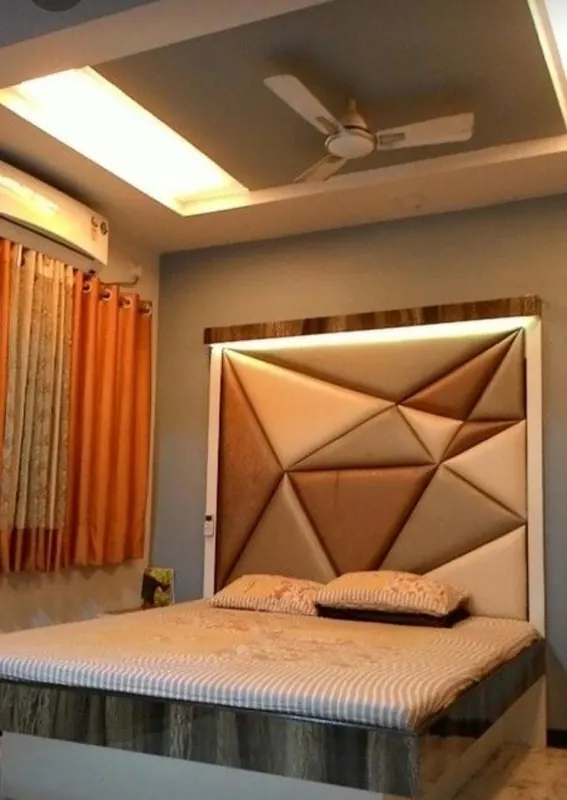 Beige geometric triangle-panelled headboard with a backlit cove, in a bedroom with orange curtains