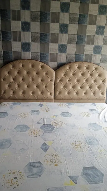 Pair of beige diamond-tufted arched headboards against patchwork wallpaper