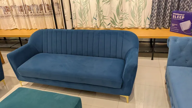 Blue velvet three-seater sofa with a channel-tufted back and brass legs, in the Gouri Furnishing showroom