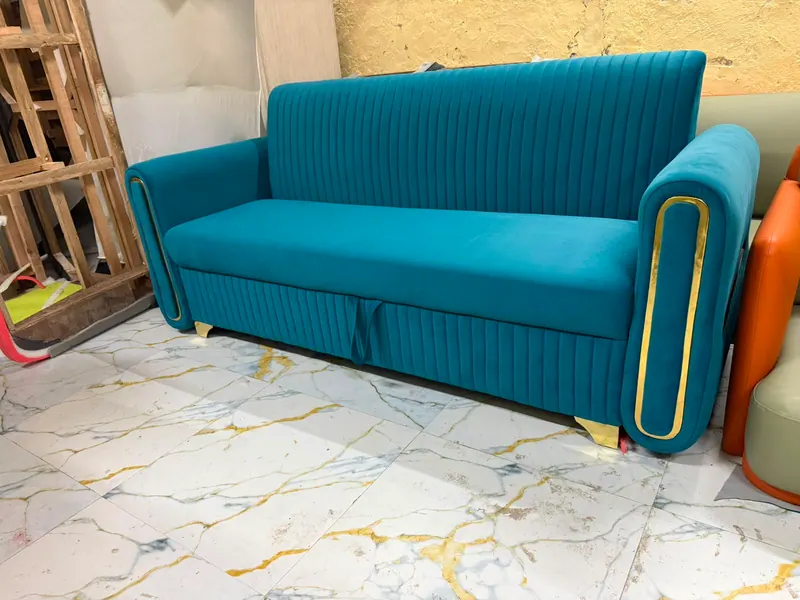 Teal velvet sofa cum bed with gold trim on the arms, finished in the Thane workshop