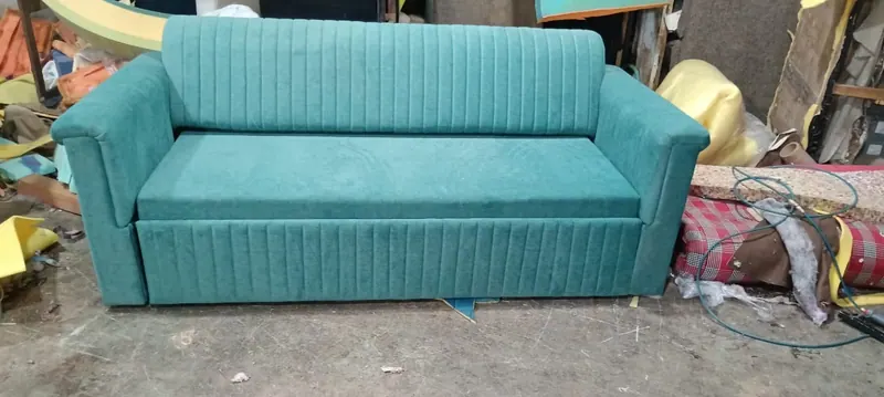 Teal sofa cum bed mid-build on the workshop floor, showing the fluted base construction