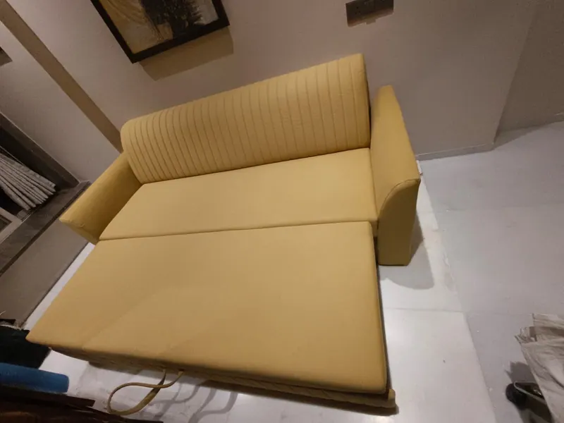 Pale yellow sofa cum bed opened flat, showing the fold-out mattress section
